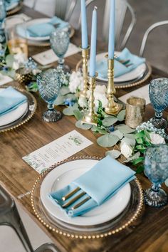 the table is set with blue and white plates, napkins, silverware, and candles