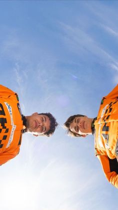 two men in orange jerseys standing next to each other looking up at the blue sky