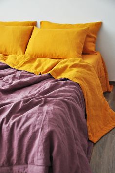 an unmade bed with yellow and purple linens on the bottom, along with two pillows