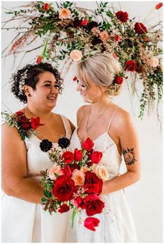 two women standing next to each other with flowers in their hair and holding bouquets