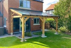 a wooden gazebo sitting on top of a lush green field next to a brick building