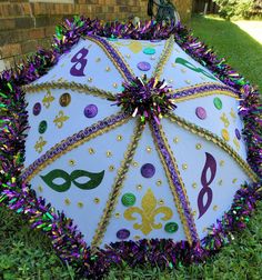 a white umbrella with mardi gras decorations on it sitting in the grass next to a brick wall