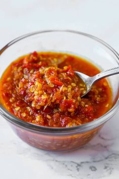 a spoon in a glass bowl filled with chili sauce