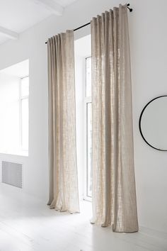 a white room with curtains and a round mirror hanging on the wall next to it