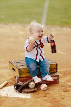 a small child sitting on top of a wooden crate holding a bottle and baseball bat