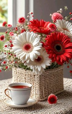 red and white flowers in a basket next to a cup of coffee on a table