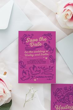 the wedding stationery is set on top of white envelopes and pink flowers are in front of it