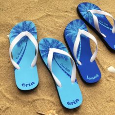 three pairs of blue and white flip flops laying on the sand next to shells