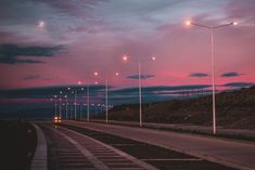 an empty road with street lights on both sides at sunset or dawn in the evening