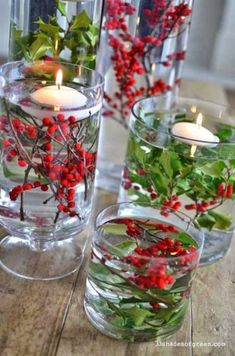 three glass vases filled with red berries and greenery on top of a wooden table