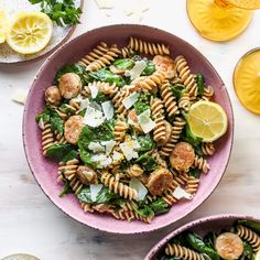 two pink bowls filled with pasta salad next to lemons and lime slices on the side