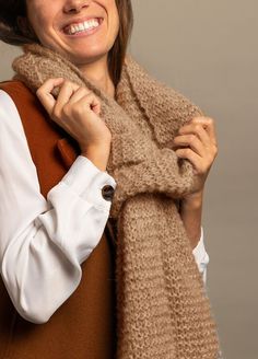 a woman is smiling and wearing a brown scarf over her shoulders with a white shirt underneath