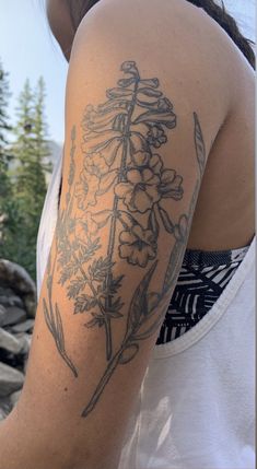 a woman's arm with flowers on it and trees in the back ground behind her