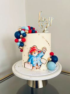 a birthday cake with an image of a teddy bear on the top and balloons around it