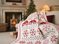 a christmas quilt is on display in front of a fire place with a lit fireplace