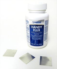 a bottle of handy flux next to two pieces of metal and one piece of mirror