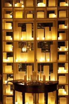 many candles are lit in front of a wall with glass blocks on it and one candle is sitting on top of the table