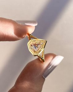 a woman's hand holding a ring with a yellow diamond in the middle and white nail polish