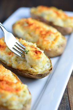 a fork is stuck into baked potatoes on a white plate with another potato in the background