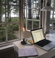 an open laptop computer sitting on top of a desk next to a candle and window