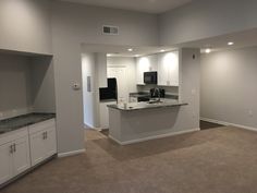 an empty kitchen and living room in a new home with white cabinets, granite counter tops, and black appliances