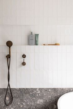 a bathroom with white tile walls and flooring next to a bathtub, shower head, and sink