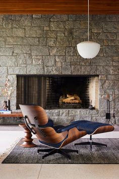 an eames chair and ottoman in front of a stone wall with a fire place