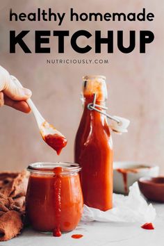 a person holding a spoon full of ketchup next to two jars filled with sauce