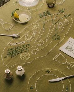 the table is covered with embroidered designs and utensils, including lemons, limes, and other items