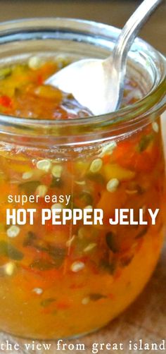 a jar filled with hot pepper jelly on top of a wooden table next to a spoon