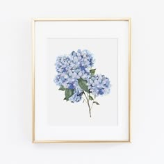 a blue hydrangea flower is displayed in a gold frame on a white wall