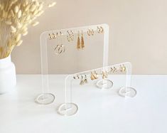 three clear acrylic jewelry stands with earrings on them and a vase full of dried flowers