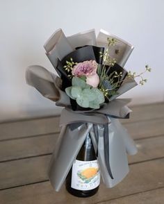 a wine bottle wrapped in grey paper with flowers and leaves on the top, sitting on a wooden table