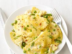 a white plate topped with pasta covered in cheese and peas next to a silver fork