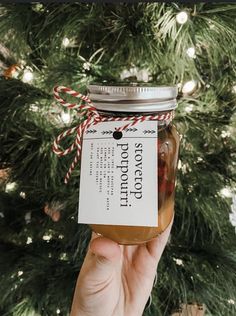 a hand holding a jar filled with food next to a christmas tree