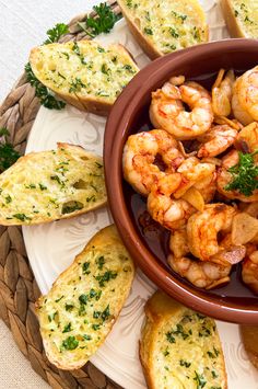 a bowl filled with shrimp and bread on top of a white plate next to garlic bread