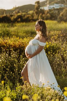 a pregnant woman in a white dress walking through the grass