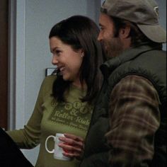 a man and woman standing next to each other in front of a door holding coffee mugs