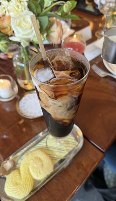 there is a drink on the table with some cookies and flowers in the vase behind it