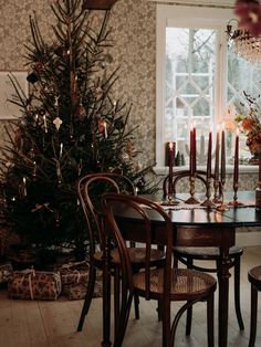 a dining room table and chairs with candles on it in front of a christmas tree