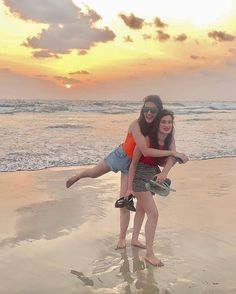 two girls are playing on the beach at sunset