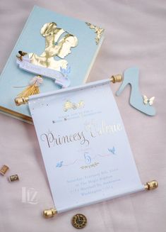 the princess's welcome card is next to some gold and blue decorations on a pink table cloth