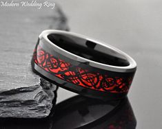 a wedding ring with red and black inlays sits on top of a rock