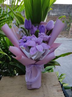 a bouquet of purple flowers sitting on top of a wooden table next to green plants