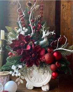 a white vase filled with red ornaments and greenery on top of a wooden table