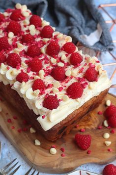 a cake with white frosting and raspberries is on a wooden platter