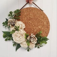 a hand holding a cork board with flowers and leaves hanging on the side of it