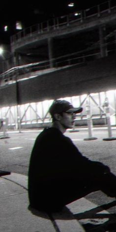 a man sitting on top of a metal bench next to a parking lot at night