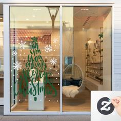 a store front window with christmas decorations on the glass and a hand holding a pen