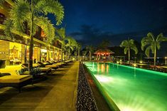 an outdoor swimming pool at night with lounge chairs and palm trees in the foreground